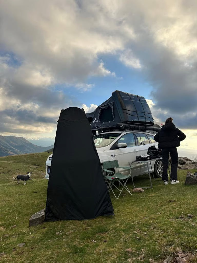 Un SUV blanc équipé d'une tente de toit rigide, garé sur une crête panoramique, avec un abri