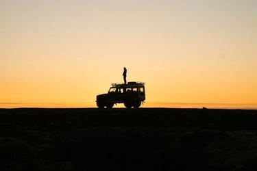 Silhouette d'une personne debout sur un 4x4 au coucher du soleil, lors d'un voyage d'aventure 